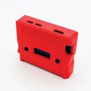May include: A bright red rectangular electronic device case with a small blue screen and several ventilation slots. The case has a textured surface and two black circular buttons. The design is angular and modern.