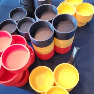 Op de afbeelding: Een set kleurrijke, stapelbare, ronde containers. De containers zijn in drie kleuren: rood, geel en blauw. De containers zijn in een driehoekige vorm gerangschikt.