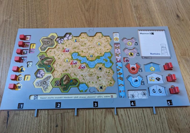 K&ouml;nnte beinhalten: Ein Brettspiel mit einem grauen Spielbrett mit einer sechseckigen Karte mit Gel&auml;nde, Wasser und Geb&auml;uden. Enth&auml;lt rote und blaue Spielsteine ​​und eine wei&szlig;e Karte mit Text. Das Spielbrett hat die Zahlen 1-5 unten.