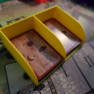 Pu&ograve; includere: Un porta carte in plastica gialla con due scomparti per contenere le carte. Le carte hanno illustrazioni del sole, della luna e delle nuvole. Il testo "events" &egrave; stampato su una delle carte.