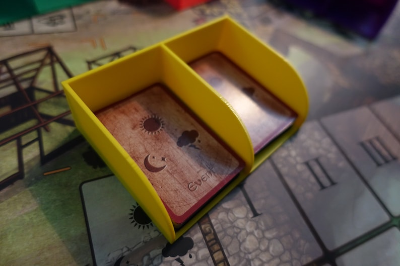 Pu&ograve; includere: Un porta carte in plastica gialla con due scomparti per contenere le carte. Le carte hanno illustrazioni del sole, della luna e delle nuvole. Il testo "events" &egrave; stampato su una delle carte.