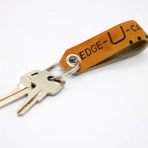 May include: A tan leather keychain with the text "EDGE-U-CA" and two silver keys attached.