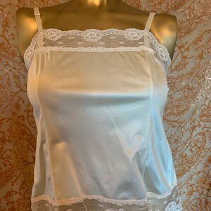 May include: Ivory-colored camisole with adjustable straps and delicate lace trim along the neckline and hem. The camisole is made of a smooth, satin-like fabric. The lace features a floral pattern.