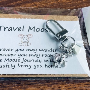 May include: A silver moose keychain with a small silver charm attached. The keychain is packaged in a clear plastic bag with a brown card that reads "Travel Moose" and a poem about safe travels.