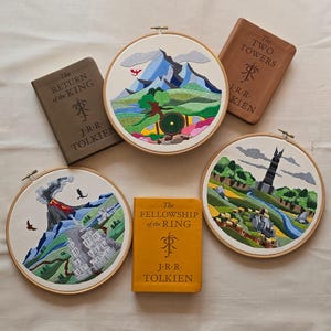 Puede incluir: Un surtido de aros bordados y libros con escenas y títulos de "El Señor de los Anillos" de J.R.R. Tolkien. Los aros representan paisajes con montañas, un volcán y una torre. Los libros son marrones y amarillos.