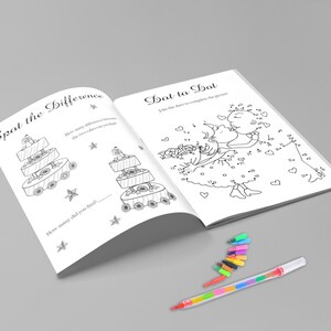 May include: Open activity book with two pages: "Spot the Difference" and "Dot to Dot". The "Spot the Difference" page shows two similar cakes. The "Dot to Dot" page features a drawing of two people kissing. A multi-colored pen and several small markers are on the surface.