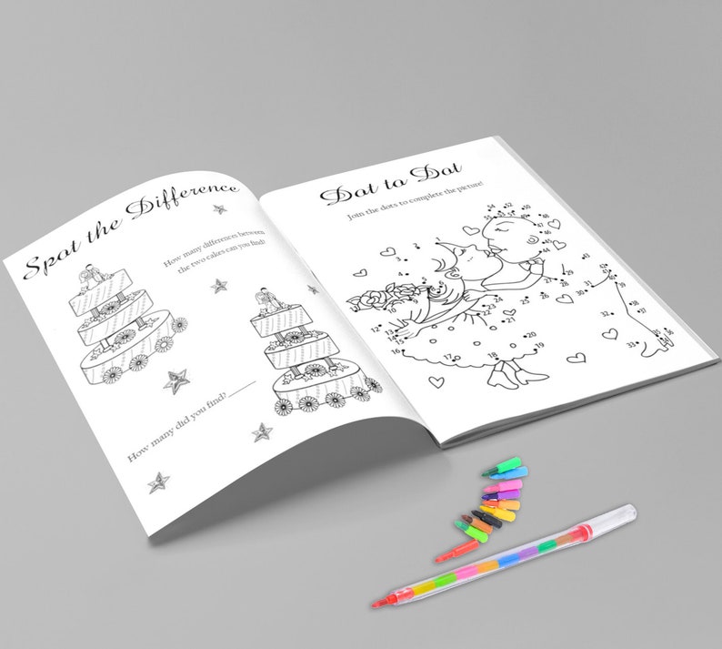 May include: Open activity book with two pages: "Spot the Difference" and "Dot to Dot". The "Spot the Difference" page shows two similar cakes. The "Dot to Dot" page features a drawing of two people kissing. A multi-colored pen and several small markers are on the surface.