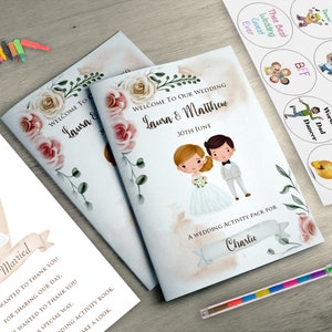 May include: Wedding activity pack with a cartoon bride and groom illustration. The cover reads "Welcome to Our Wedding" and includes the names "Laura & Matthew" and the date. Includes stickers and a multi-colored pen.