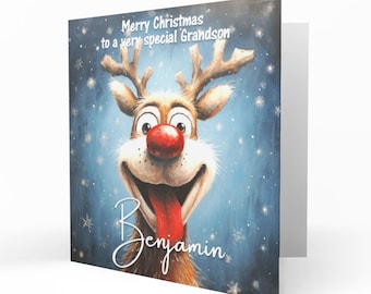 Può includere: Un biglietto d'auguri quadrato con una renna dei cartoni animati dal naso rosso brillante e la lingua di fuori su uno sfondo blu innevato. Il testo recita Merry Christmas to a very special Grandson e il nome Benjamin in corsivo bianco.
