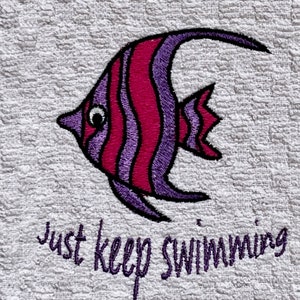 May include: A white towel with a purple and pink embroidered fish and the text "just keep swimming".