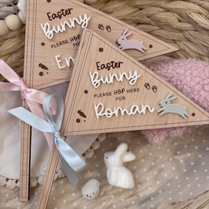 May include: Two wooden Easter bunny signs with the text "Easter Bunny Please Hop Here For" and the names "Emma" and "Roman". The signs are decorated with bunny footprints and a bunny silhouette.