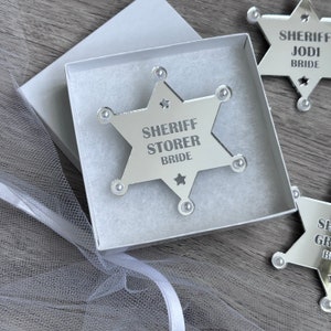 May include: A silver star-shaped sheriff's badge with the text "SHERIFF STORER BRIDE" in a white box.