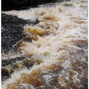 May include: A scenic view of a river with rushing water. The water is a mix of brown and white, creating a foamy texture. Dark rocks and trees frame the water, creating a natural landscape.