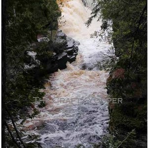 May include: A view of a rushing waterfall cascading over rocks, with lush green trees framing the scene.