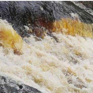 May include: A close-up of a waterfall with white and yellow water cascading over dark gray rocks.