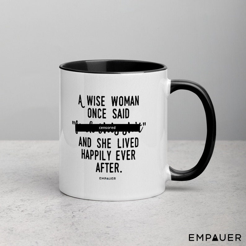 May include: White coffee mug with a black rim and handle. The mug has a black text design that reads "A wise woman once said "censored" and she lived happily ever after." The text "EMPAUER" is printed in black at the bottom of the mug.