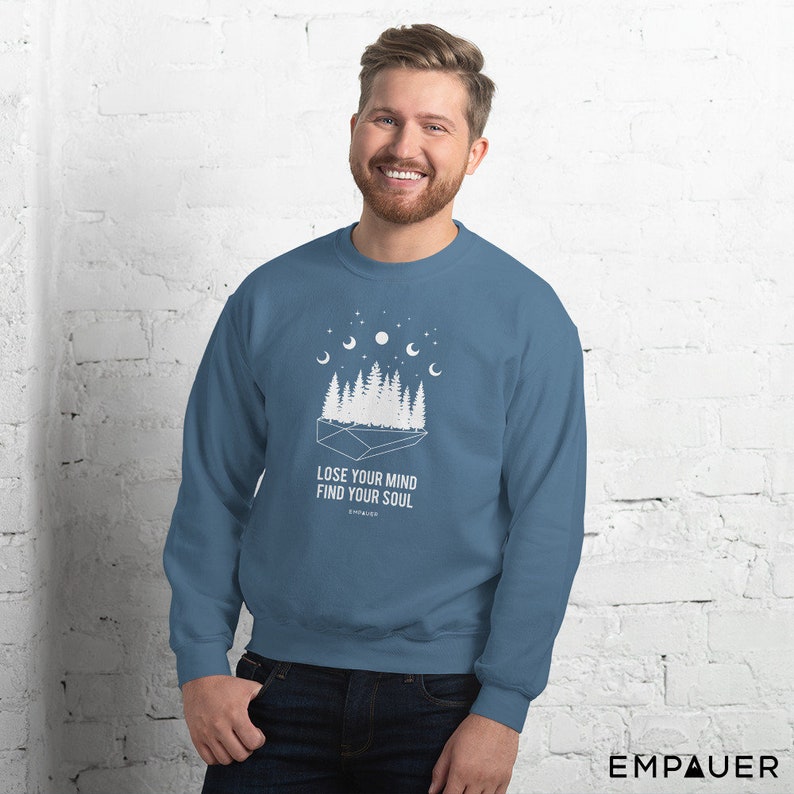 K&ouml;nnte beinhalten: Blaues Sweatshirt mit wei&szlig;er Grafik eines Waldes, Monden und Sternen. Der Text "LOSE YOUR MIND FIND YOUR SOUL" ist darunter gedruckt. Das Sweatshirt hat einen Rundhalsausschnitt.