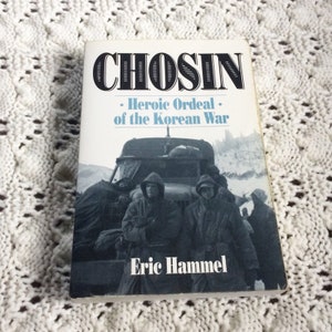 May include: A book titled "Chosin: Heroic Ordeal of the Korean War" by Eric Hammel. The cover features a black and white photo of soldiers in a truck during a snowy winter.