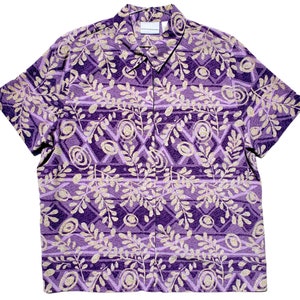 May include: Purple and gold short-sleeved button-down shirt with a floral pattern. The shirt has a collar and a button-up front.