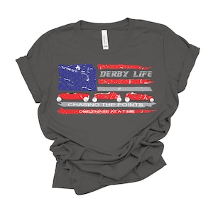 May include: A dark gray t-shirt with a red, white, and blue American flag design. The flag has three red race cars with the text "Derby Life" and "Chasing the Points One Phase at a Time" printed below.