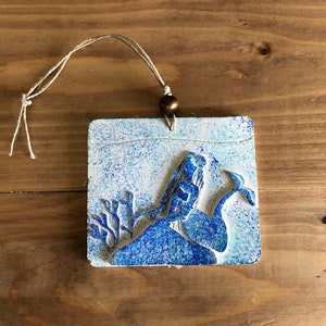Peut inclure: Une décoration en céramique bleue et blanche avec un motif de baleine et de corail. La décoration est munie d'une ficelle pour l'accrocher.