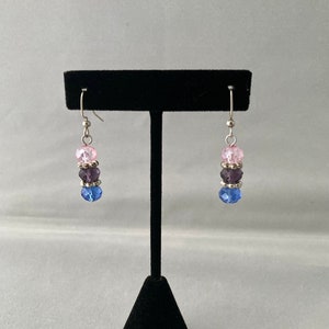 May include: A pair of dangle earrings with three crystal beads each. The beads are pink, purple, and blue.
