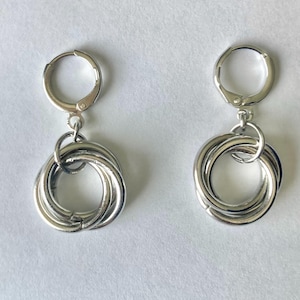 Puede incluir: Un par de pendientes de aro de plata con un diseño trenzado. Los pendientes están hechos de varios anillos entrelazados.