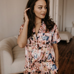 May include: A pink satin pyjama set with a short-sleeved top and shorts. The fabric features a print of various dog breeds in different poses.