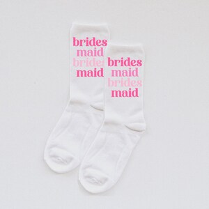 May include: Two white socks with the phrase "brides maid" repeated on each sock in pink lettering.