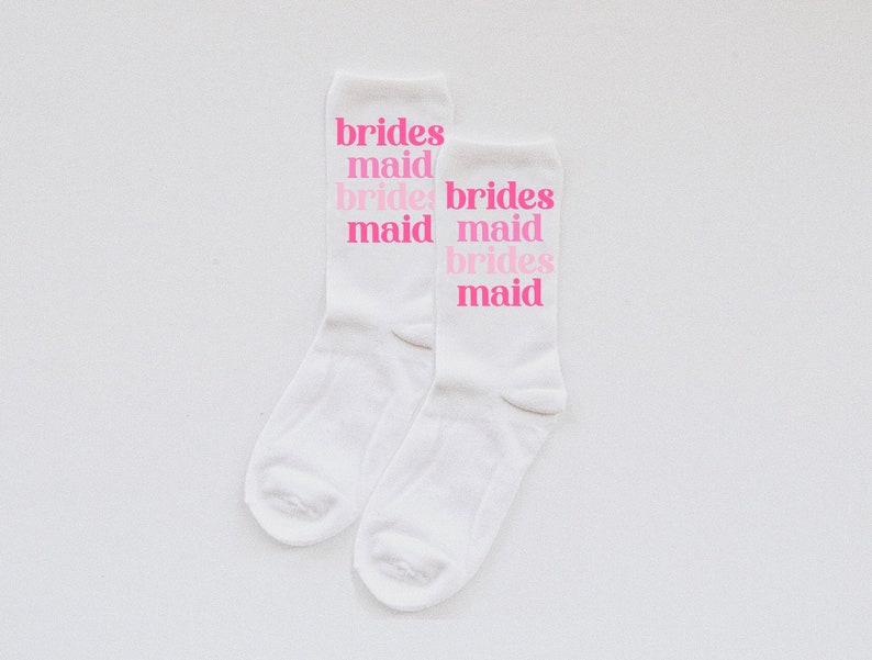 May include: Two white socks with the phrase "brides maid" repeated on each sock in pink lettering.