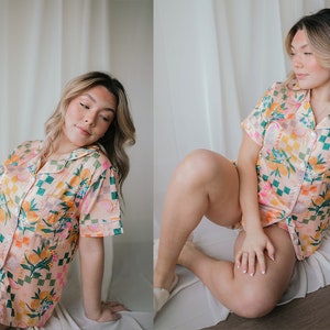May include: A woman wearing a pink and green floral short-sleeved pyjama top and matching shorts. The pyjamas have a checkered pattern and feature a variety of floral and fruit designs.