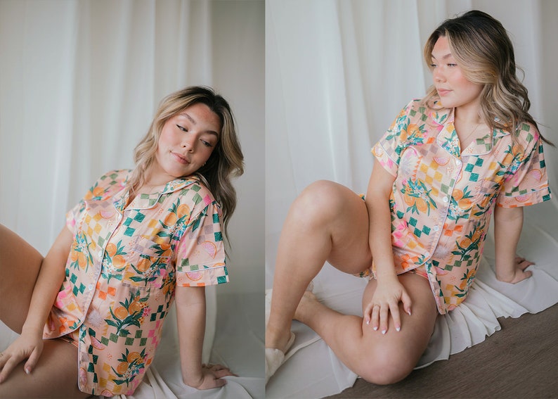 May include: A woman wearing a pink and green floral short-sleeved pyjama top and matching shorts. The pyjamas have a checkered pattern and feature a variety of floral and fruit designs.
