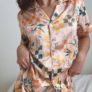 May include: A peach-coloured satin pyjama set with a checkered pattern and a citrus fruit print. The set includes a short-sleeved button-up top and matching shorts.