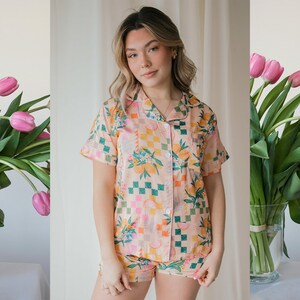 May include: A pink and orange pyjama set with a checkered and floral print. The top has short sleeves and a button-up front. The shorts have a matching print.