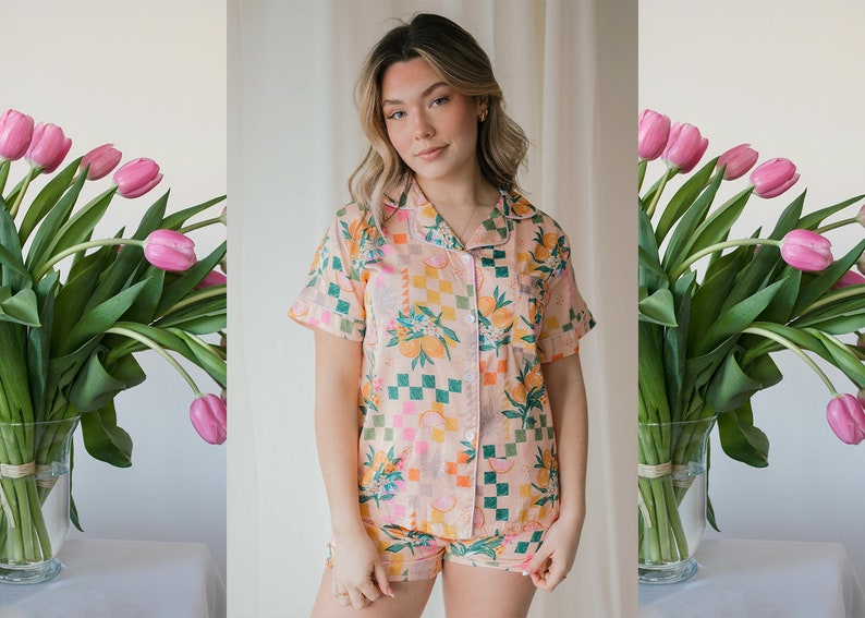 May include: A pink and orange pyjama set with a checkered and floral print. The top has short sleeves and a button-up front. The shorts have a matching print.