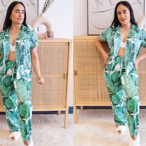 May include: Green and white pajama set with a tropical leaf pattern. The set includes a short-sleeved button-down shirt and matching pants. The pajamas are made of a lightweight fabric and are suitable for sleepwear or loungewear.