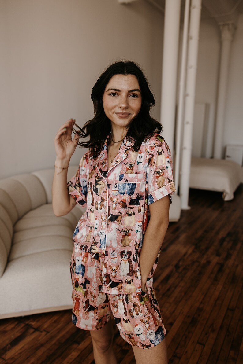 May include: A pink and white pyjama set featuring a print of various dog breeds. The set includes a short-sleeved shirt and shorts.
