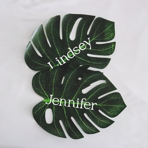 May include: Two green monstera leaves with the names Lindsey and Jennifer written in white on them.