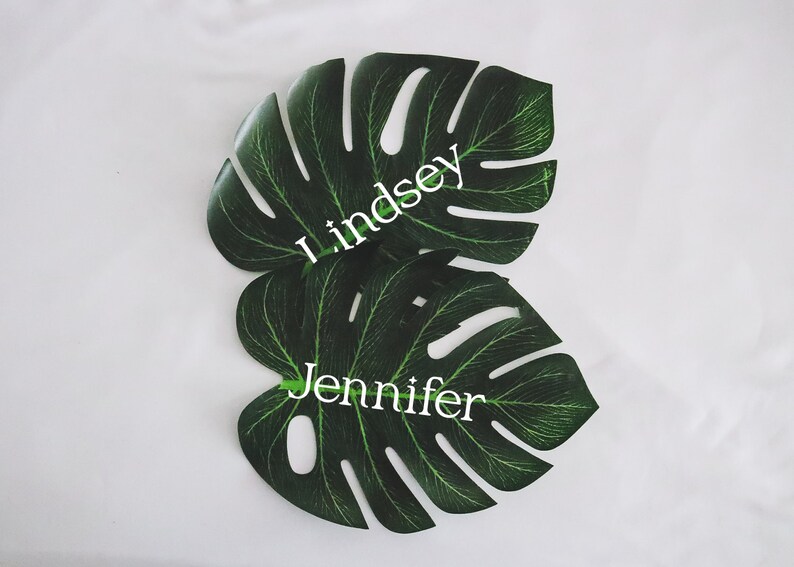 May include: Two green monstera leaves with the names Lindsey and Jennifer written in white on them.