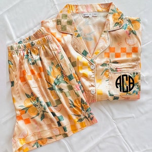 May include: A peach-coloured pyjama set with a lemon and chequered pattern. The top has a button-up front and a pocket with a monogrammed "ACB" on it.