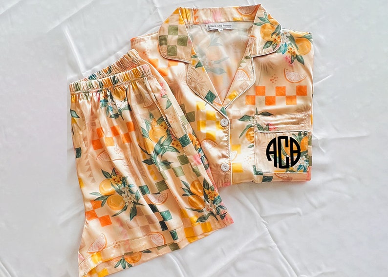 May include: A peach-coloured pyjama set with a lemon and chequered pattern. The top has a button-up front and a pocket with a monogrammed "ACB" on it.
