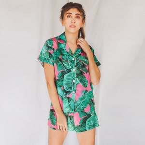 May include: A pink and green tropical print pajama set with short sleeves and shorts. The top has a button-up front and a collar.