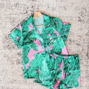 May include: Pink and green tropical print pajama set with short sleeves and shorts. The top has a button closure and the shorts have an elastic waistband. The top has the name "Jen" embroidered on the chest.