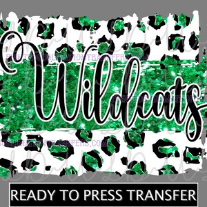 May include: A ready-to-press transfer featuring the word "Wildcats" in black script over a green glitter stripe. The design includes a white background with green and black leopard print accents.