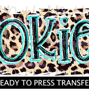 May include: A leopard print design with the word "OKIE" in black and turquoise lettering. The text "READY TO PRESS TRANSFER" is in a black rectangle at the bottom. This design is suitable for apparel and crafts.