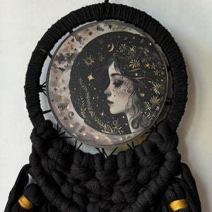May include: Black macrame dreamcatcher with gold accents. The centre features a round image of a woman's face with a crescent moon and stars. The text "@Content Spirit" is at the bottom of the image.