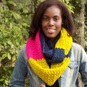May include: A vibrant, crocheted infinity scarf in pink, navy, and yellow. The scarf is handmade with a textured stitch, creating a cosy and stylish accessory. This item is perfect for adding a pop of colour to any outfit.