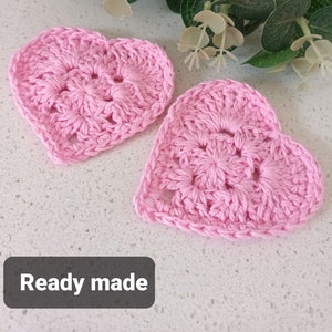 May include: Two pink crocheted hearts, ready made. The hearts are made with a delicate stitch pattern and have a slightly raised texture.