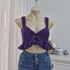 Puede incluir: Un top de crochet morado con un lazo en la parte delantera y un dobladillo con volantes.