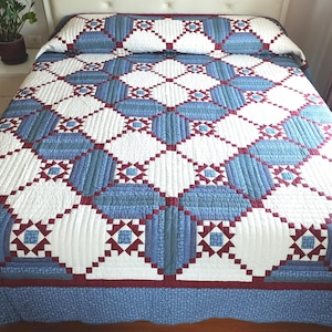 Puede incluir: Un edredón hecho a mano con un patrón geométrico en blanco, azul y burdeos. El edredón presenta un diseño repetitivo de cuadrados y rectángulos, creando una ropa de cama visualmente atractiva y acogedora. El edredón está colocado sobre una cama.